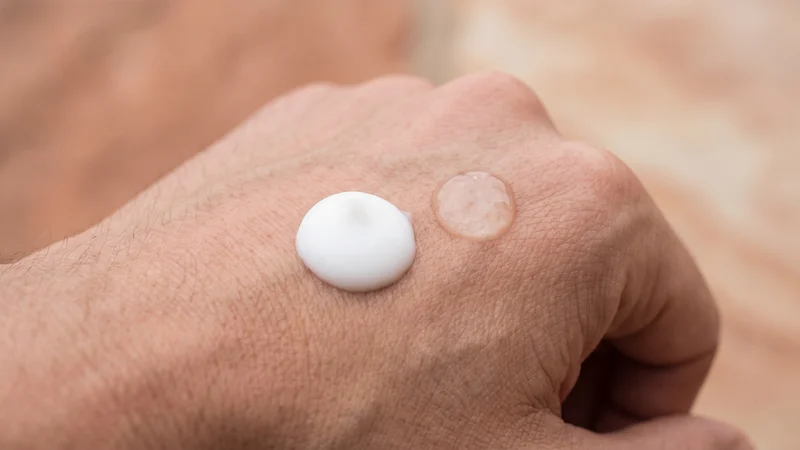Texture d'un baume après-rasage blanc et d'une lotion transparente sur le dos de la main
